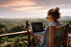 woman sitting on balcony with laptop on lap and view of trees in the distance