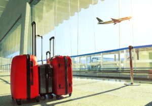 two red suitcases and a gray suitcase sitting in airport with airplane flying by window in background
