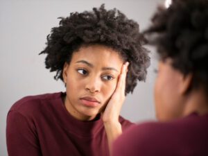 a young african american woman looks at herself in the mirror with a sad expression