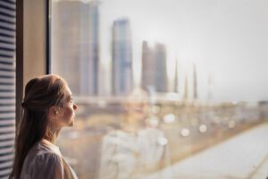 a woman with light hair and pale skin is looking out a window at a city skyline